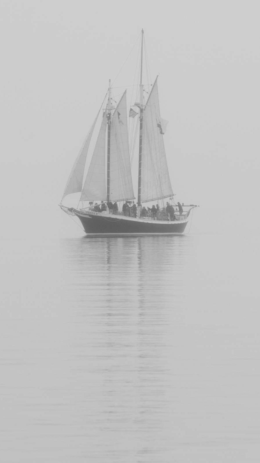 a black and white scene with a sailboat on the water surrounded my heavy fog